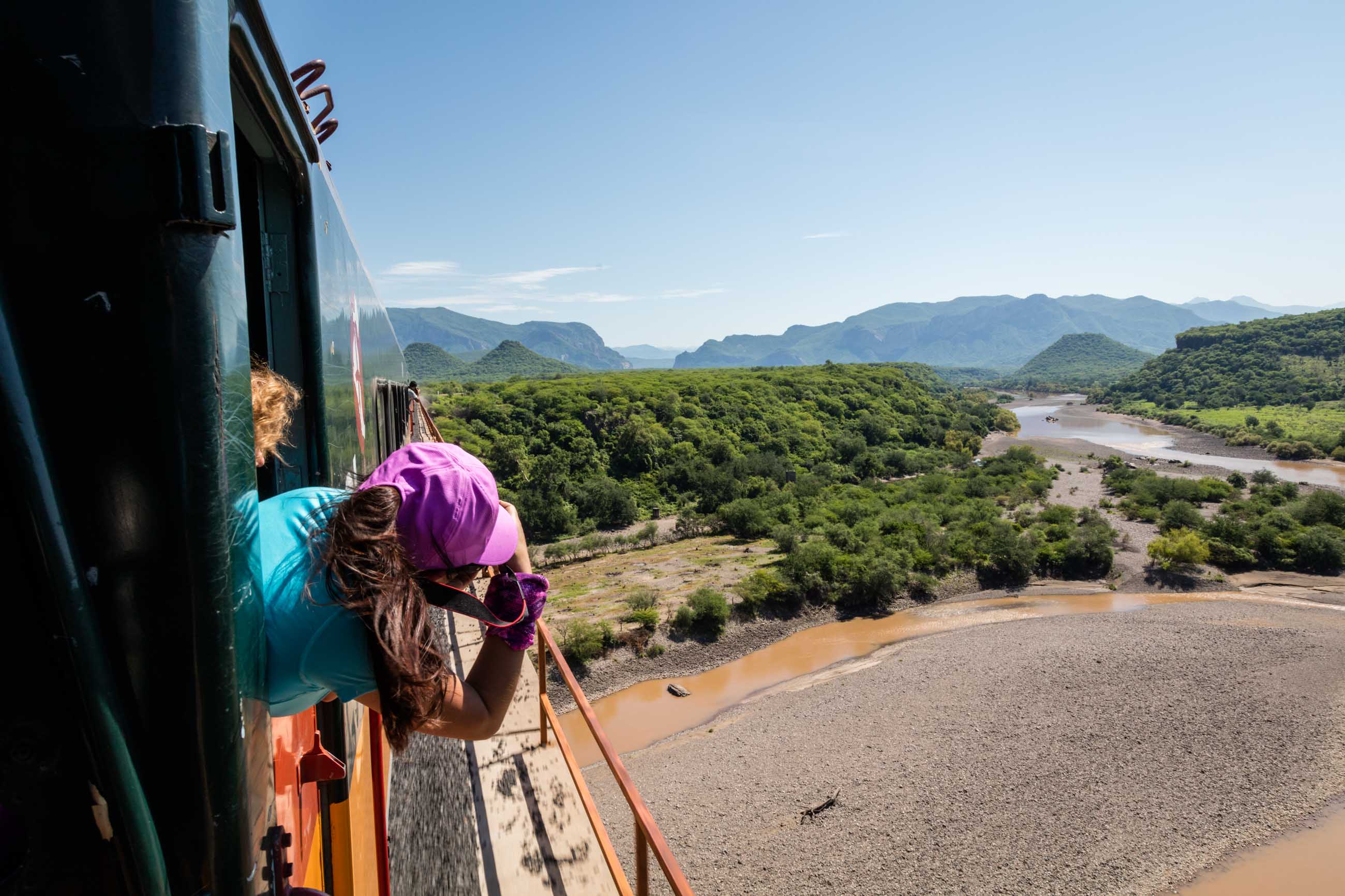 Una pasajera asomada por la ventana del Chepe Regional mientras el tren cruza un puente sobre el río.